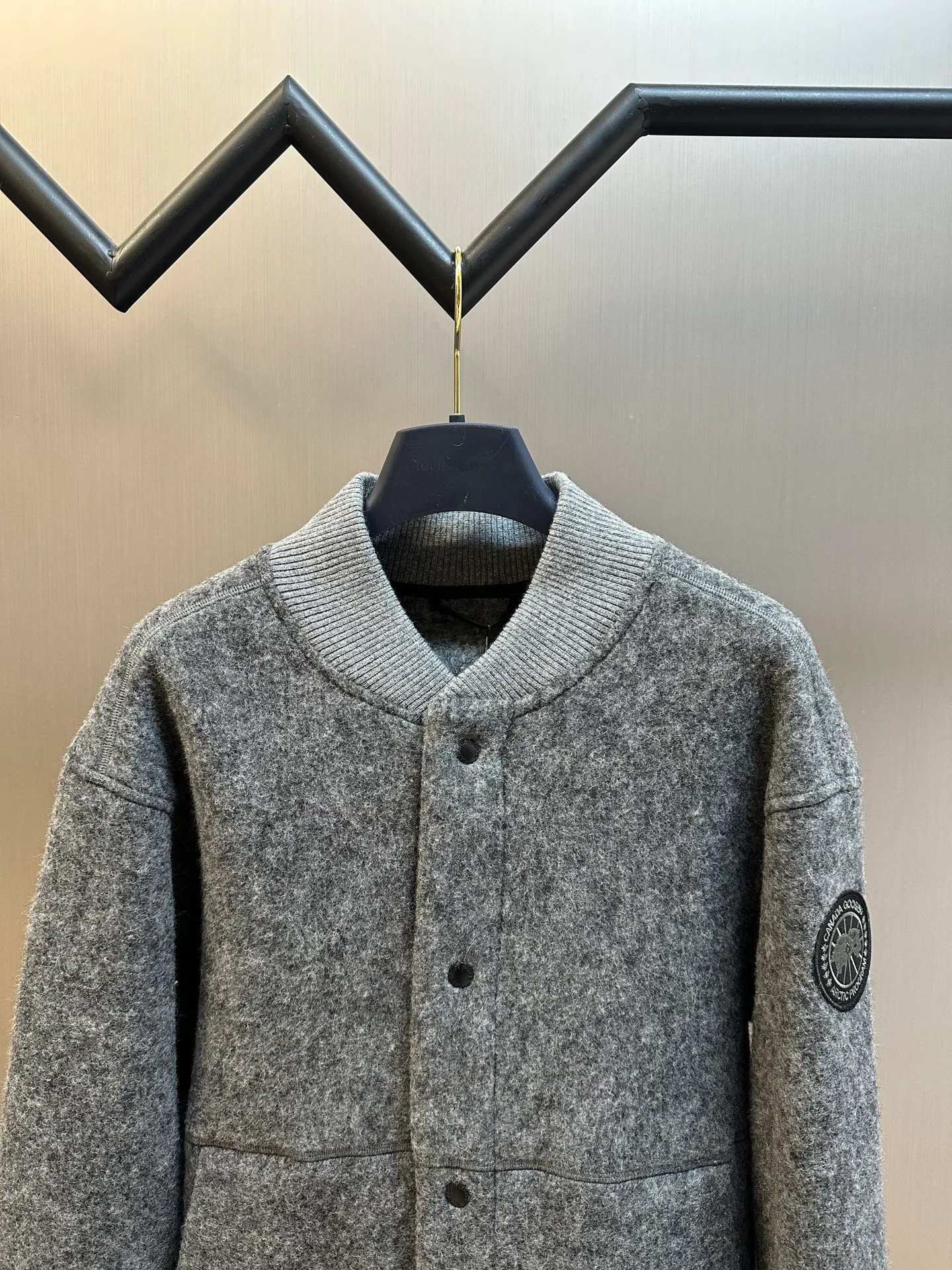 P770 Canada Goose Fleece Badge Button Jacket The main fabric of this jacket is light gray wool blend fabric to improve the fabric's wear resistance, wrinkle resistance and warmth. Wool provides good warmth and a natural feel, while blended fibers enhance the fabric's practicality and durability.  The cutting process needs to ensure that the texture and color of the fabric are evenly distributed, especially with this light gray tone, to avoid chromatic aberrations. The stretchability of wool-blend fabrics needs to be taken into consideration when cutting pieces to ensure dimensional stability of the finished garment.  Use a sewing needle and thread suitable for wool-blend fabrics to avoid damage to the fabric during sewing. The sewing stitches are even and firm to prevent thread stripping.  The temperature needs to be controlled during ironing to avoid high temperature damage to the fabric while keeping the fabric smooth and crisp. The front and back body parts, sleeves and other main parts are stitched with flat seams to ensure a smooth silhouette. Align the fabric texture at the splices to keep the look neat.  The white circular armband on the left arm is an important part of the brand identity and is finely sewn to ensure it is strong and flat.  size：s m l xl